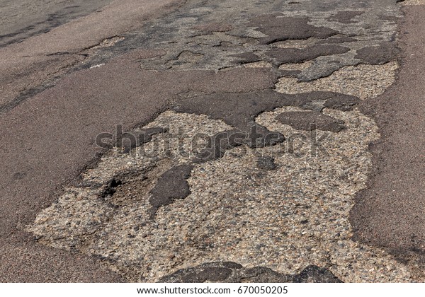 Damaged asphalt road\
with potholes. Bad road. Repair. Patch repair of asphalt. Bad\
asphalt, dangerous road, Broken automobile road, cracks, holes,\
potholes in asphalt\
