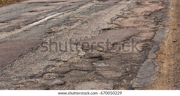 Damaged asphalt road\
with potholes. Bad road. Repair. Patch repair of asphalt. Bad\
asphalt, dangerous road, Broken automobile road, cracks, holes,\
potholes in asphalt\
