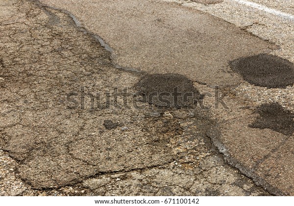 Damaged\
asphalt road with potholes. Bad road. Pitch Repair. Repair of\
asphalt repair. Bad asphalt, dangerous road, Broken automobile\
road, cracks, holes, potholes in the\
asphalt