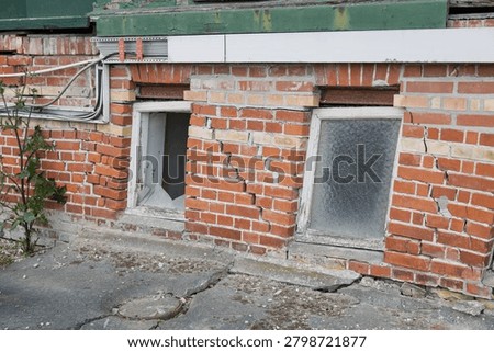 Damaged brick wall with broken windows and cracked pavement.