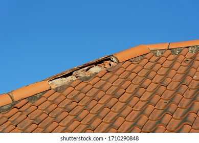 Damaged broken ridge roof tiles against a blue sky