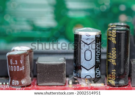 Damaged capacitor on a circuit board. Top is bulged out showing failure. Undamaged capacitors also present. No brand markings. Shallow depth of field.