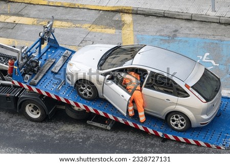 Damaged car being loaded onto tow truck by a worker. Towing service on the city. Roadside assistance concept