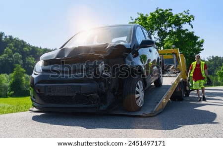 Damaged car being towed onto a flatbed tow truck with operator walking behind. Roadside assistance concept image