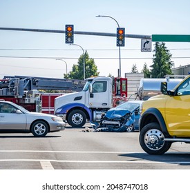 Damaged cars after a car accident crash involving a big rig semi truck with semi trailer at a city street crossroad intersection with traffic light and rescue services to help the injured