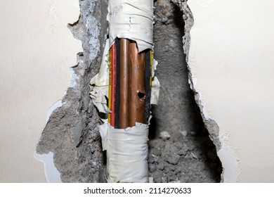 Damaged Copper Pipe In A Wall Surrounded By Various Wires And Pipes