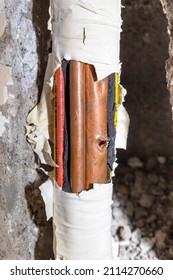 Damaged Copper Pipe In A Wall Surrounded By Various Wires And Pipes