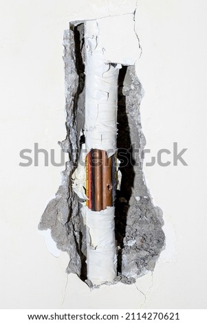 Damaged copper pipe in a wall surrounded by various wires and pipes