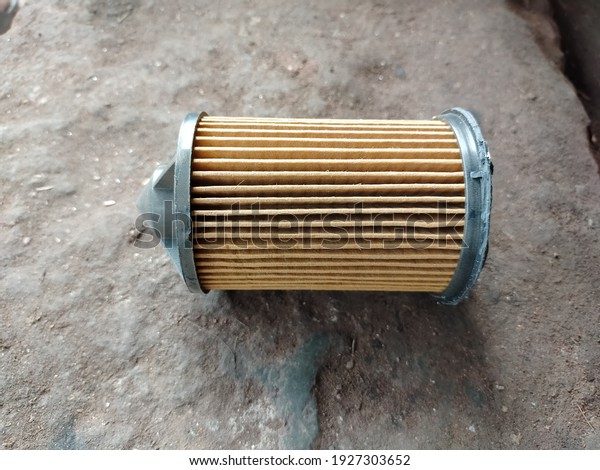 Damaged and dusty car oil filter isolated on\
ground background. Broken and dirty auto filter isolated on ground.\
Motorcycle air filter
