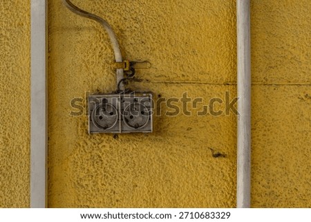 Damaged electrical socket on a dirty yellow wall, damaged electrical installation, electricity theft, illegal 220V installation