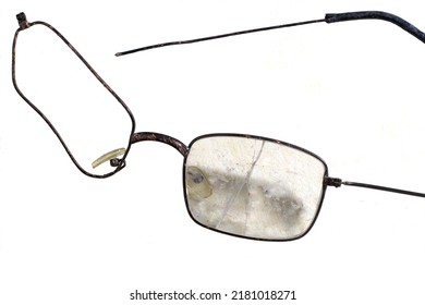 Damaged Eyeglasses With A Bent Frame Detached Temple Missing Right Lens And Heavily Scratched And Cracked Left Lens On A White Surface.