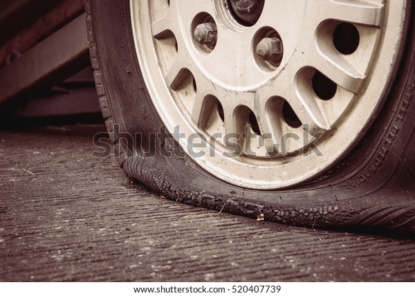 Damaged flat tire of an old car on\
the road with selective focus and vintage filter\
effect