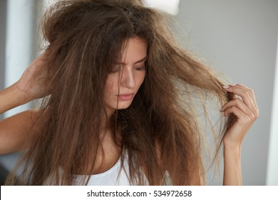 Damaged Hair. Beautiful Sad Young Woman With Long Disheveled Hair. Closeup Portrait Of Female Model Holding Messy Unbrushed Dry Hair In Hands. Hair Damage, Health And Beauty Concept. High Resolution