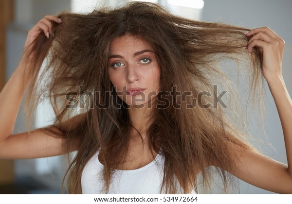 ダメージヘア 髪の毛が乱れた美しい悲しい若い女性 汚いブラシをかけない乾いた髪を手に持つ女性モデルの接写 ヘアダメージ 健康 美容のコンセプト 高解像度 の写真素材 今すぐ編集