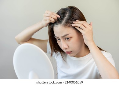 Damaged Hair, face serious asian young woman worry looking at scalp in mirror, hand in break into front hair loss, thin problem symptom at home. Health care shampoo beauty, isolated on background.
