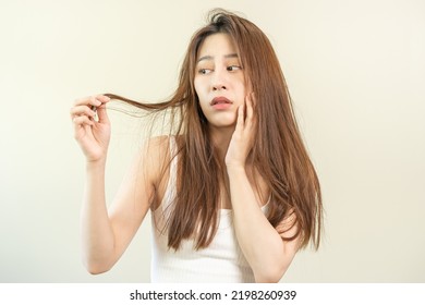 Damaged Hair, frustrated asian young woman, girl hand in holding splitting ends, messy unbrushed dry hair with face shock, long disheveled hair, health care of beauty. Portrait isolated on background. - Shutterstock ID 2198260939