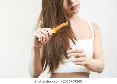 Damaged Hair, frustrated asian young woman, girl hand in holding brush splitting ends messy while combing hair, unbrushed dry long hair. Health care beauty, portrait isolated on white background. - Shutterstock ID 2366759245
