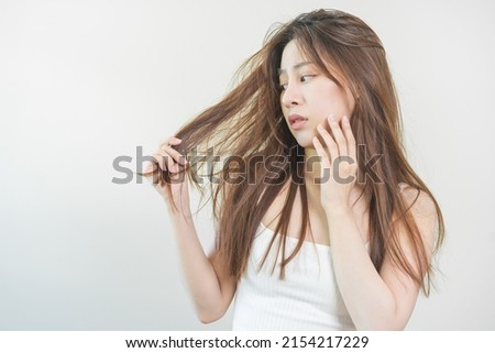 Damaged Hair, frustrated asian young woman, girl hand in holding splitting ends, messy unbrushed dry hair with face shock, long disheveled hair, health care of beauty. Portrait isolated on background.