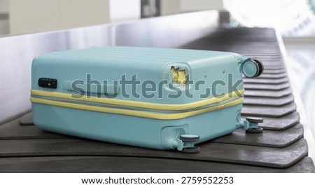 Damaged hard shell suitcase with hole and visible interior on baggage conveyor belt in airport close up view.