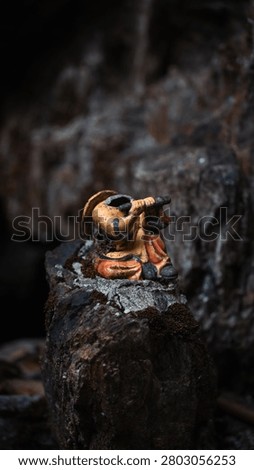 Damaged headless miniature ceramic statue of a musician playing the flute on a dark mossy rock in a cave shrine