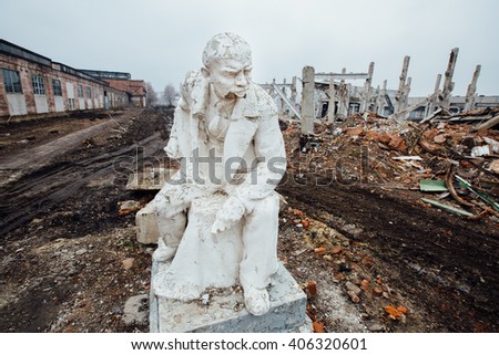 Damaged Lenin statue sitting on a chair with a book in his hand. peeling vintage paint. ruins of the factory background. The concept of system failure