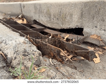 A damaged and mangled metal storm drain grate on a street in San Marcos.
