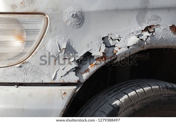 Damaged old front car wing with rust, holes and\
scratches, close-up\
photo
