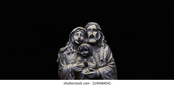 Damaged old sculpture of a beautiful small happy nuclear family of father, mother and child isolated on a black background with copy space. Gives us a spooky scary feeling. Closeup macro side view.