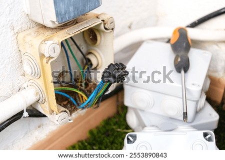 A damaged outdoor electrical cable box is being replaced with a new unit. The old box shows signs of wear, while the new installation awaits connections to ensure safe operation.