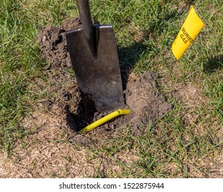 Damaged Plastic Natural Gas Line From Digging Hole In Soil In Yard With Shovel. Yellow Buried Gas Warning Flag. Concept Of Notify Utility Locating Company For Underground Utilities Before Digging