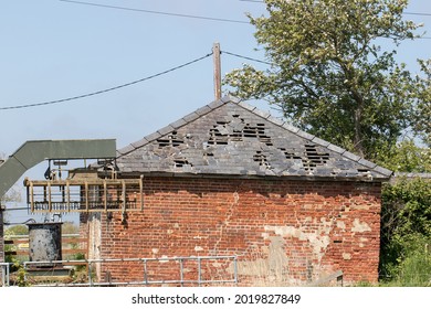 Damaged Roof And Wall. Slate Tiles Falling Off Derelict Agricultural Building. Hole In Roof Of Outbuilding. Restoration Project With Leaking Roof Of Neglected Brick Building In Need Of Repair.