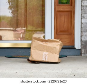 A Damaged Shipping Cardboard Box Is On A Door Step In Front Of A House For An Insurance Or Warranty Concept.