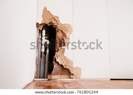 Damaged wall exposing burst water pipes after flood