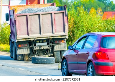 Damaged wheel hub and truck tire as a result of the accident. Broken truck loaded with gravel on the side of the road waiting for maintenance. Road traffic. - Shutterstock ID 2207392581