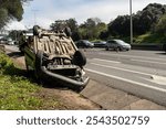 Damaged wrecked car after collision lying upside down on roadside. Busy city street with car rolled over during daytime. Car accident 