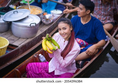 Damnoen Saduak Floating Market tourists visiting by boat popular attractions on canals of Ratchaburi, Thailand. Merchant sell fruits, agricultural produce, and Thai cuisine on the wooden boat. 