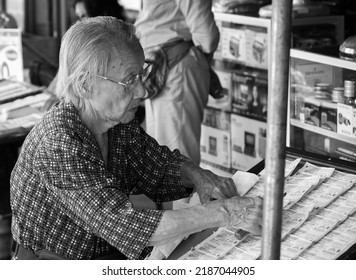 Damnoen Saduak, Thailand, 1 July 2015 8.37, An Old Woman Organizing A Lottery Stall, Black And White