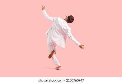 Dance Like No One Is Watching. Full Length Studio Shot Of Happy Elated Young Man Dancing And Having Fun. Back View Of Funny Guy In White Suit Dancing Isolated On Solid Pastel Pink Colour Background