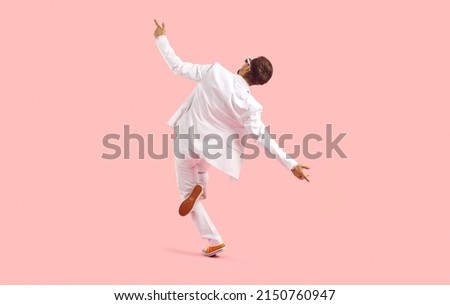 Dance like no one is watching. Full length studio shot of happy elated young man dancing and having fun. Back view of funny guy in white suit dancing isolated on solid pastel pink colour background