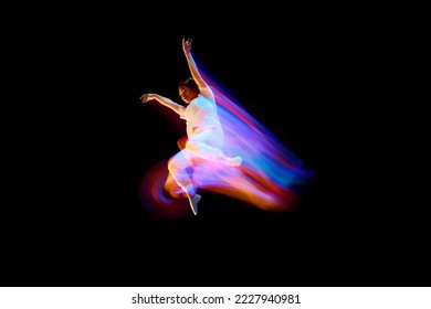 Dance in motion. Studio shot of flying, jumping dancer or gymnast performing tricks in the air over black background with mixed neon glowing rays. Fantasy, cyberpunk, sport, fashion