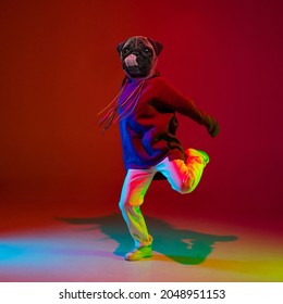 Dance moves. Young man, hip hop dancer headed of dog's head dancing isolated over dark red background in neon light. Inspiration, idea, street dance style. Surrealism, ad. Contemporary artwork
