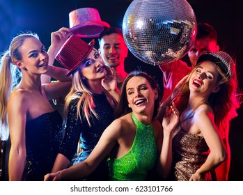 Dance Party With Group People Dancing . Women And Men Have Fun In Night Club. Happy Girl On Foreground And Disco Ball On Background. Guys Took Off Their Hats.