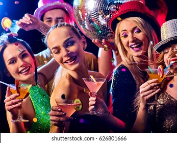 Dance Party With Group People Dancing . Women And Men Have Fun And Drinking Martini Cocktail In Night Club. Happy Girl On Foreground And Disco Ball On Background. Guys Took Off Their Hats.