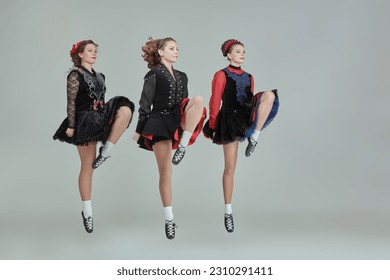 Dance prformance. Professional women's Irish dance ensemble in concert costumes and Ghillies Soft Shoes dance together in a row. Full-length studio portrait on a grey background. - Shutterstock ID 2310291411