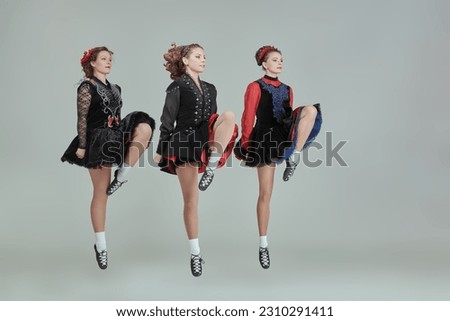 Dance prformance. Professional women's Irish dance ensemble in concert costumes and Ghillies Soft Shoes dance together in a row. Full-length studio portrait on a grey background.