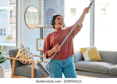 Dance, radio or woman cleaning with music for singing or listening to a song with broom as a guitar at home. Relax, freedom or happy Indian girl cleaner streaming audio on headphones or housekeeping