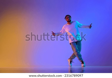 Dance show. Young guy dancing contemp, breakdance and hip-hop against gradient multicolored studio background in neon light. Concept of street style dance, fashion, youth, hobby, dynamics, ad
