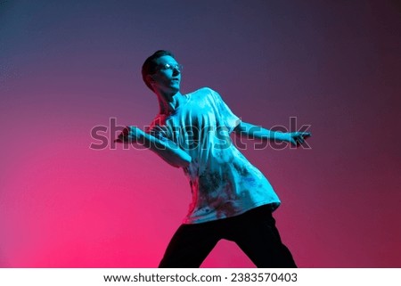 Dance studio. Expression. Young Caucasian male hip-hop dancer practising isolated over gradient pink purple background in neon light. Concept of dance, youth, hobby, dynamics, movement, action, ad