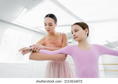 Dance Teacher Assisting Preteen Girl Learning In Ballet School