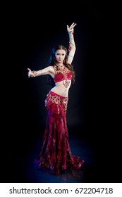 Dancer brunette girl with long hair in red oriental costume posing and dancing on black background in studio